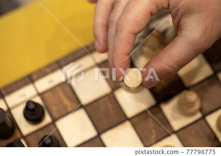 Hand taking next step on chess game. Human hand moving wooden white rook piece Hand taking next step on chess game. Human hand moving wooden white rook piece 77798775