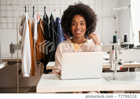 Woman looking to the camera while working at her laptop computer Woman looking to the camera while working at her laptop computer 77799318