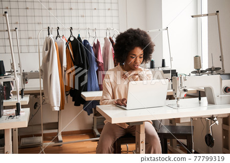 Woman looking attentively at the laptop and chatting with clients while creating 77799319