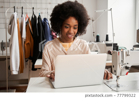 Designer working at her laptop with pleasure smile while creating new collection Designer working at her laptop with pleasure smile while creating new collection 77799322