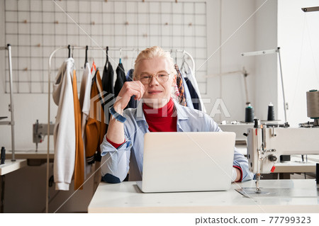 Man wearing glasses looking to the camera while working at his laptop computer Man wearing glasses looking to the camera while working at his laptop computer 77799323