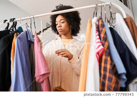 Woman looking through the hangers with clothes ready for alteration 77799343