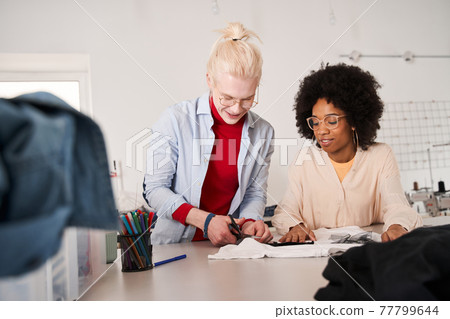 Woman looking attentively at the t shirt and listening ideas from her colleague 77799644