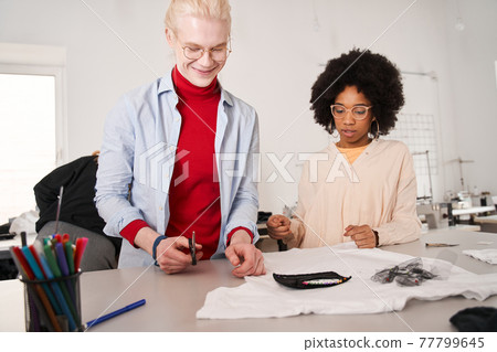 Woman looking attentively at the t shirt and listening ideas from her colleague Woman looking attentively at the t shirt and listening ideas from her colleague 77799645