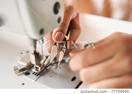 Woman cutting threads with scissors while finished re sewing clothes Woman cutting threads with scissors while finished re sewing clothes 77799690