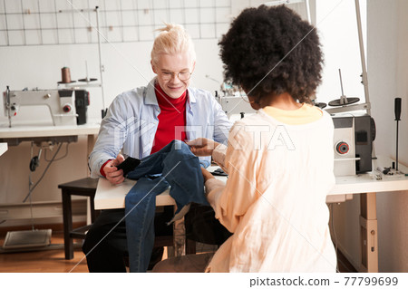 Colleagues sitting in front of each other and re sewing jeans 77799699