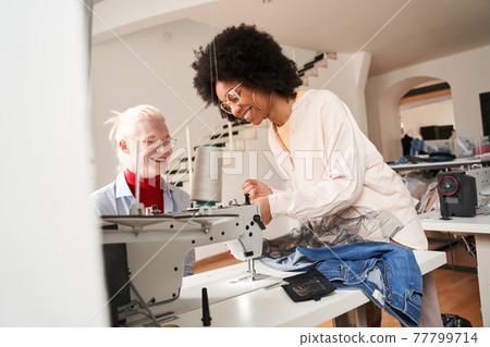 Woman critically looking at the sewing machine and smiling Woman critically looking at the sewing machine and smiling 77799714