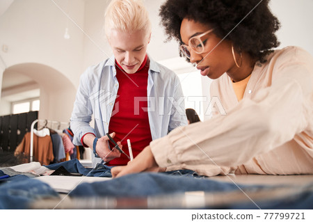 Colleagues examining jeans and drawing sketches while re sewing old clothes Colleagues examining jeans and drawing sketches while re sewing old clothes 77799721