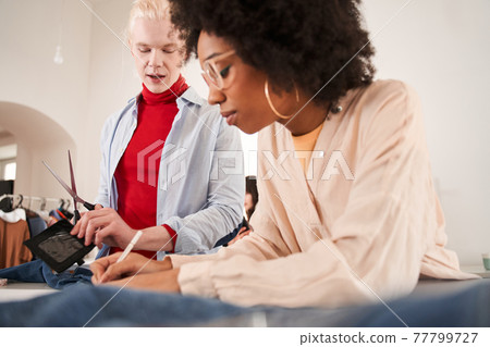 Man telling something to his multiracial colleague while re sewing Man telling something to his multiracial colleague while re sewing 77799727