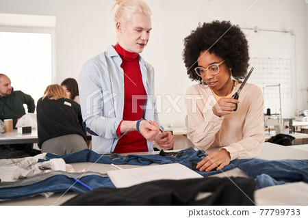 Albino man telling something to his multiracial colleague while re sewing Albino man telling something to his multiracial colleague while re sewing 77799733
