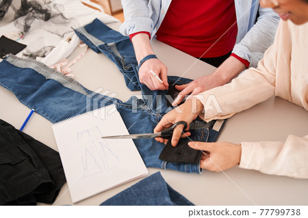 Colleagues examining jeans and drawing sketches while re sewing old clothes Colleagues examining jeans and drawing sketches while re sewing old clothes 77799738