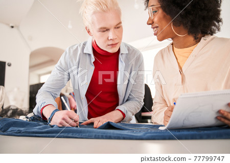 Man looking attentively at the sketch while preparing clothes to the re sewing Man looking attentively at the sketch while preparing clothes to the re sewing 77799747