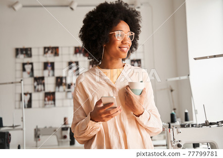 Woman holding her smartphone and looking at the window during the drinking coffee Woman holding her smartphone and looking at the window during the drinking coffee 77799781