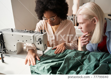 Multiracial seamstress working on the sewing machine while re sewing clothes Multiracial seamstress working on the sewing machine while re sewing clothes 77799840