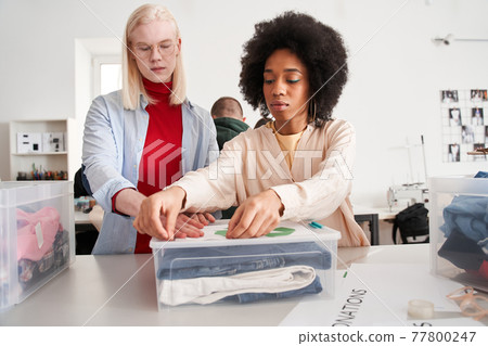 Woman sticks a recycling symbol on a plastic box with a sorting clothes 77800247