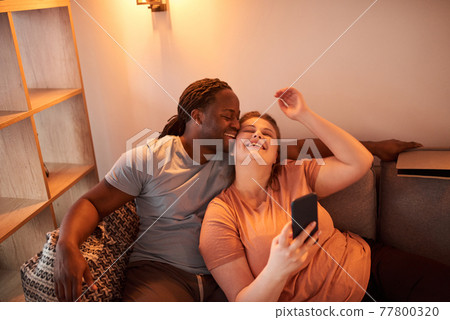 Couple bonding to each other and laughing while making selfie at the smartphone Couple bonding to each other and laughing while making selfie at the smartphone 77800320
