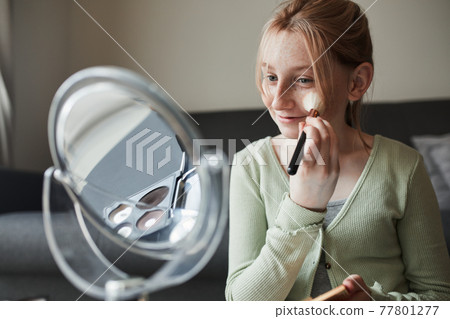 Girl looking at the mirror and preparing makeup with a powder and brush while playing 77801277