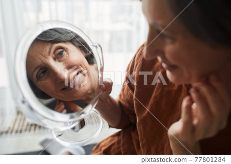 Mature woman looking at the mirror at the results of the makeup Mature woman looking at the mirror at the results of the makeup 77801284