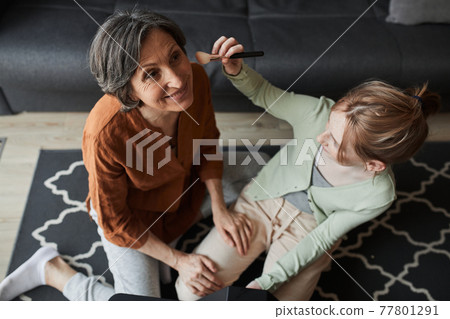 Woman sitting at the full readiness and waiting while her granddaughter preparing makeup for her Woman sitting at the full readiness and waiting while her granddaughter preparing makeup for her 77801291