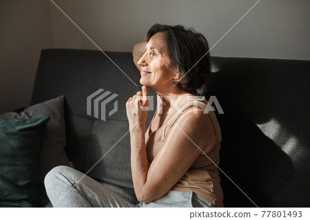Woman sitting at the sofa and looking at the window with pleasure smile 77801493