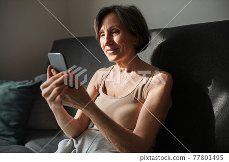 Woman wearing domestic clothes sitting at the sofa and chatting with friends 77801495