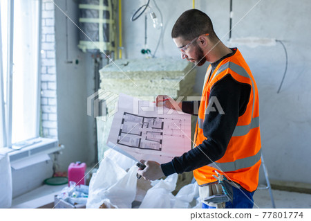 Male worker holding a paper apartment plan indoor before repair room  77801774