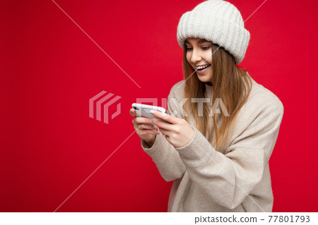 Beautiful young blonde woman wearing casual beige sweater and beige hat isolated over red background 77801793
