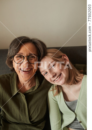 Woman laughing and bonding to her freckled granddaughter while looking to the camera 77802003