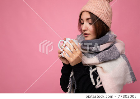 Closeup of Beautiful young brunet woman wearing black sweater hat and warm scarf isolated over pink Closeup of Beautiful young brunet woman wearing black sweater hat and warm scarf isolated over pink 77802005