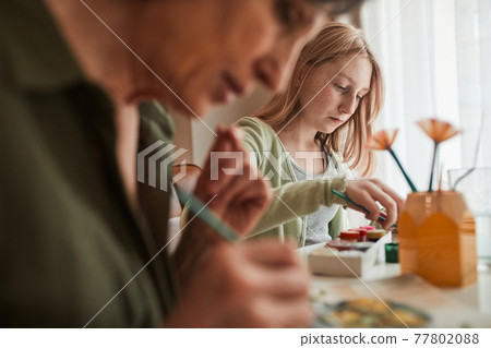Grandmother and her blonde granddaughter sitting at the table and drawing Grandmother and her blonde granddaughter sitting at the table and drawing 77802088