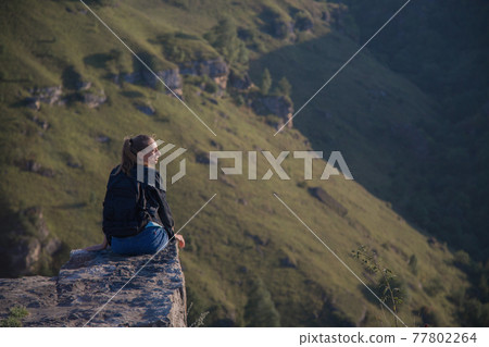 a girl with a backpack stands on the edge of a cliff. Journey through the mountains 77802264