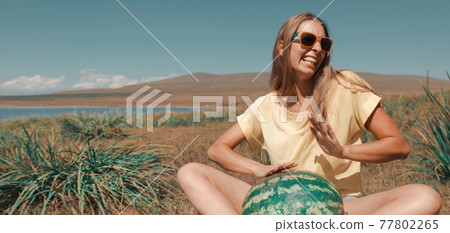 a girl sits on the beach and holds a watermelon. ripening of summer berries Joyful emotions and mood. Summer picnic. a girl sits on the beach and holds a watermelon. ripening of summer berries Joyful emotions and mood. Summer picnic. 77802265