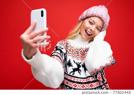 Attractive charming young smiling happy woman holding and using mobile phone taking selfie wearing Attractive charming young smiling happy woman holding and using mobile phone taking selfie wearing 77802448
