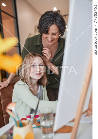 Girl looking to the camera while creating masterpiece at home with her granny Girl looking to the camera while creating masterpiece at home with her granny 77802453