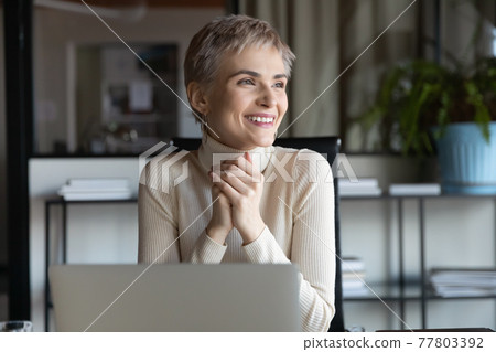 Smiling businesswoman work on laptop looking in distance 77803392