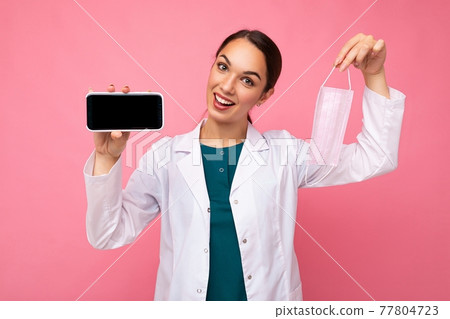 Closeup photo of smiling happy Attractive medical young woman wearing white coat holding mask 77804723