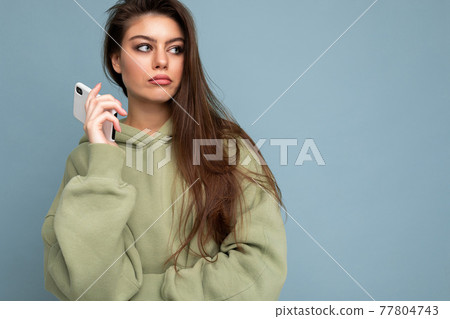 Close up of serious upset attractive young woman wearing stylish hoodie holding using mobile phone 77804743