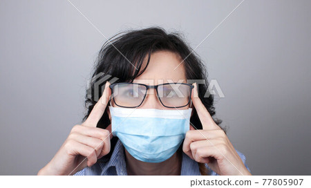 Woman wearing protection face mask against coronavirus and misted glasses. Woman in a mask looking in a mirror. 77805907