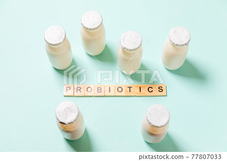 Small bottles with probiotics and prebiotics dairy drink on blue background. Production with biologically active additives. Fermentation and diet healthy food. Bio yogurt with useful microorganisms. 77807033