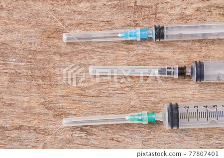 Injection needle syringes, wooden background. 77807401