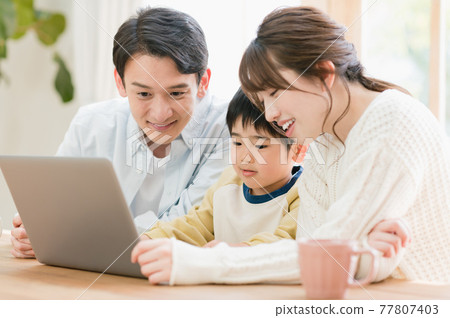 A young family sitting at a living room table and looking at a computer 77807403
