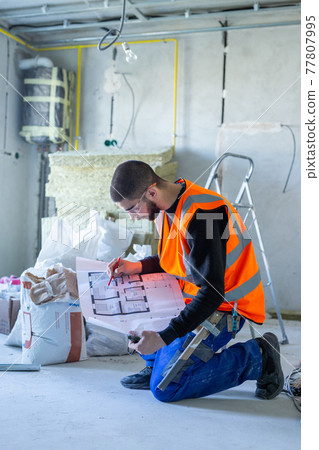 Male worker holding a paper apartment plan indoor before repair room Male worker holding a paper apartment plan indoor before repair room 77807995
