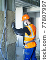 Male builder in mask putting foam into drywall 77807997