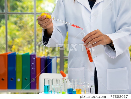 Close up scientific researcher using dropper to drop red example liquid into test tube Close up scientific researcher using dropper to drop red example liquid into test tube 77808017