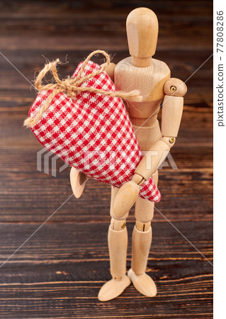 Wooden dummy holding red checkered heart. 77808286