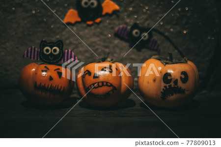 small pumpkins with different faces stand on a wooden shelf, in the background are handmade bats made of felt. Halloween Attributes 77809013