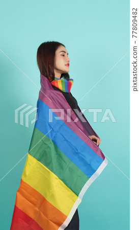 LGBTQ girl and pride flag. Sexy Lesbian girl and LGBT flag standing. blue green background. Asian LGBTQ woman with rainbow scarf on neck. Energetic cheerful. LGBTQ concept.  77809482