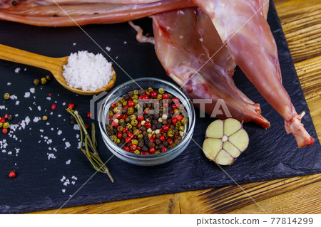 Whole raw rabbit meat with spices on a black slate cutting board on wooden table Whole raw rabbit meat with spices on a black slate cutting board on wooden table 77814299