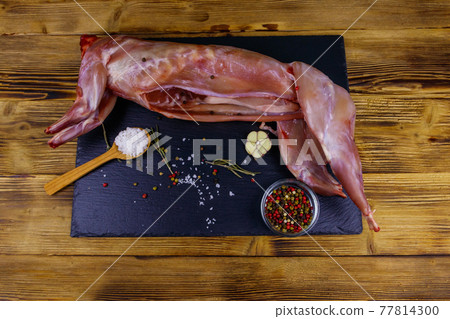 Whole raw rabbit meat with spices on a black slate cutting board on wooden table. Top view Whole raw rabbit meat with spices on a black slate cutting board on wooden table. Top view 77814300