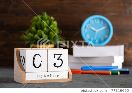 October 03rd. October 03 wooden cube calendar with blur objects on background. October 03rd. October 03 wooden cube calendar with blur objects on background. 77816630